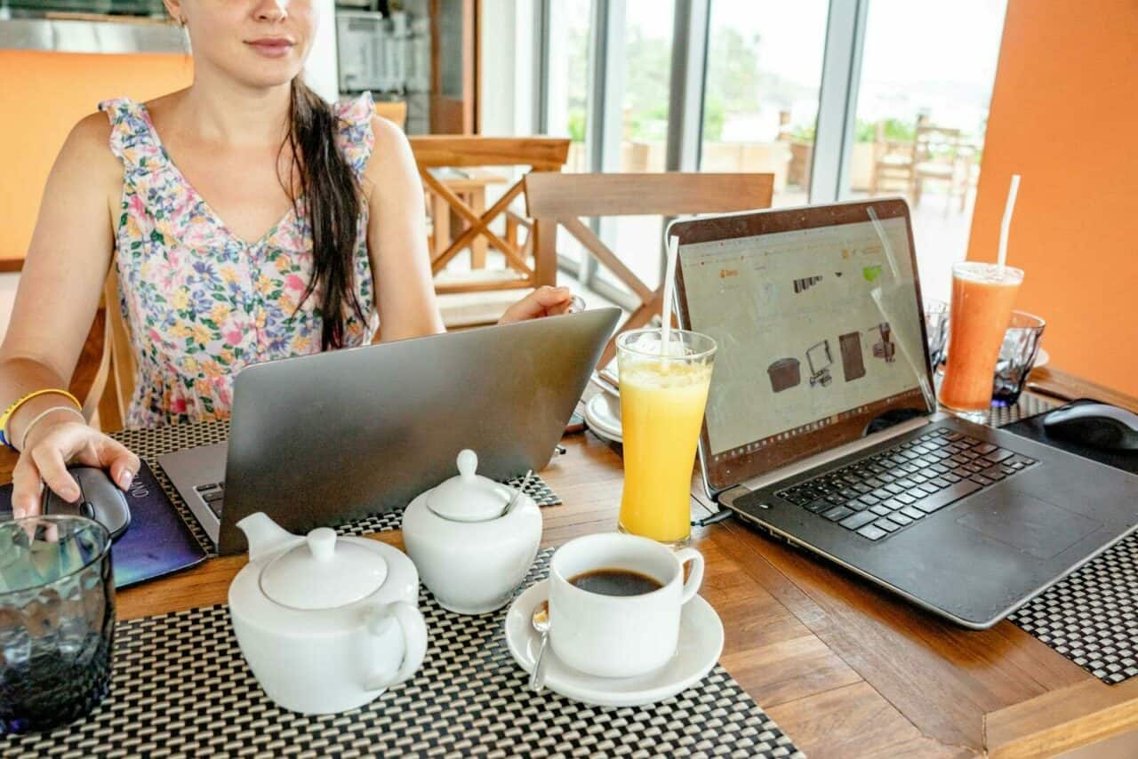 Digital nomade jobber fra kafé med laptop, nettbrett, kaffe og juice på bordet.