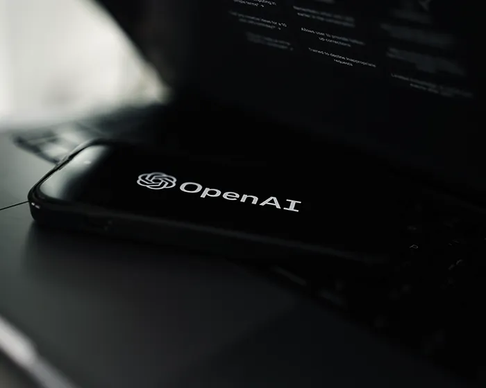 OpenAI logo displayed on a cell phone on a laptop.