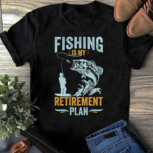 Svart T‑skjorte med motiv av en fisk som hopper ut av vannet og fiskeutstyr, med teksten «Fishing Is My Retirement Plan» i blått og gult.