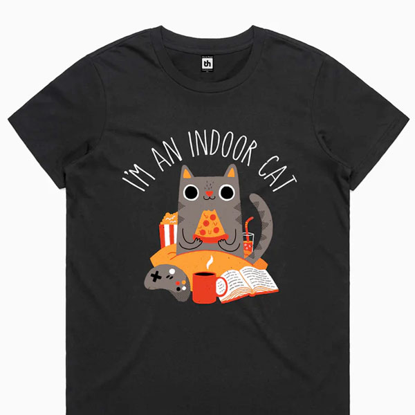 Svart T‑skjorte med koselig illustrasjon av en katt som spiser pizza i sengen, og teksten «I’m an Indoor Cat» øverst.