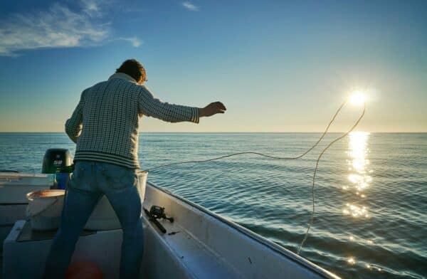 man standing on boat throwing rope on water