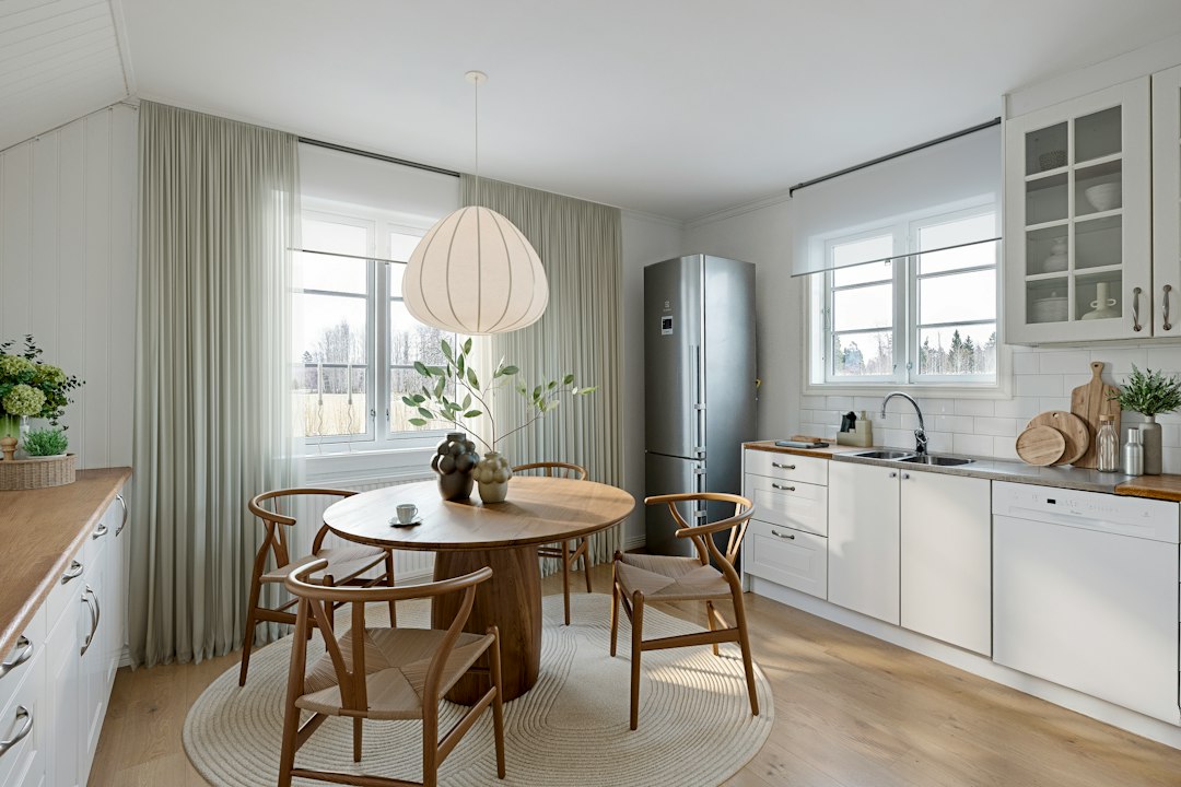 Lyst kjøkken med hvite skapfronter, spisebord i tre og en stor taklampe over bordet